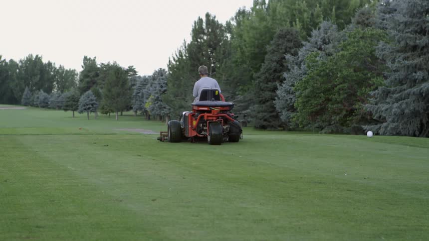 A man mows the green grass with a ride on mower