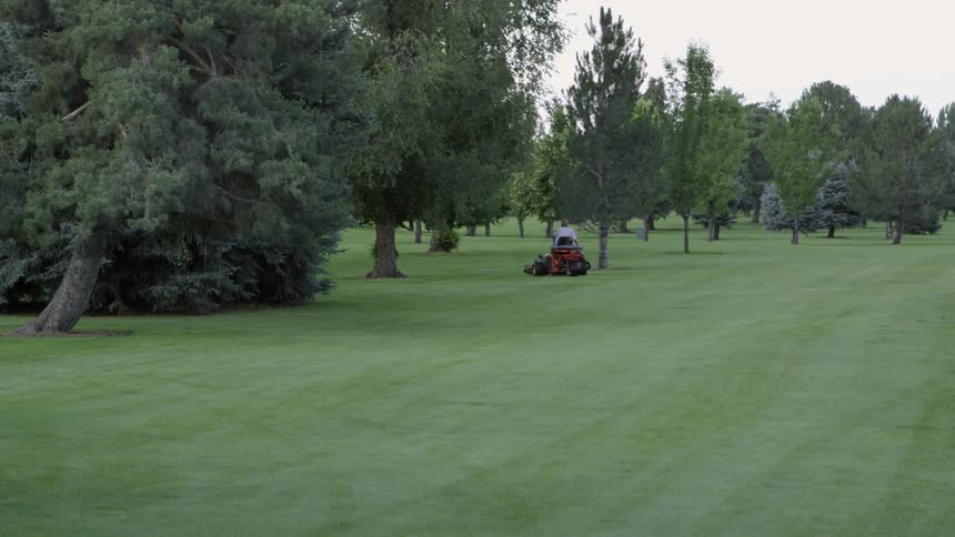 Man uses a lawnmower on a golf course at sunset