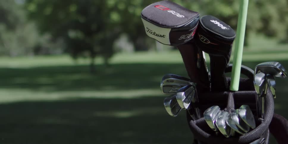 A golfers hand puts a club into a bag on the course on a sunny day