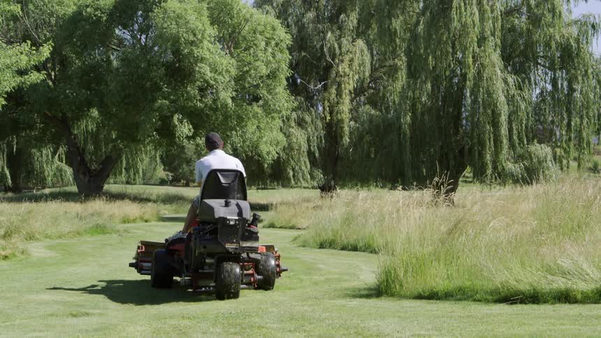 A man rides a lawn mower through a golf course