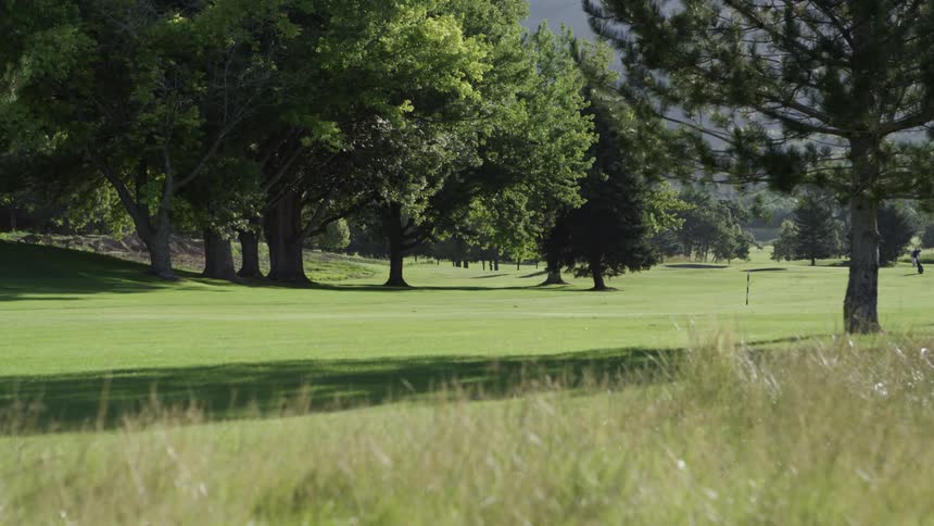 A golfer bends down to get his ball out of the hole on a bright sunny day