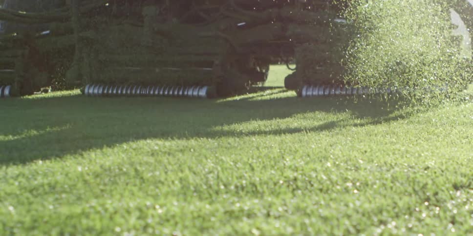 A large mower drives over the grass on a golf course