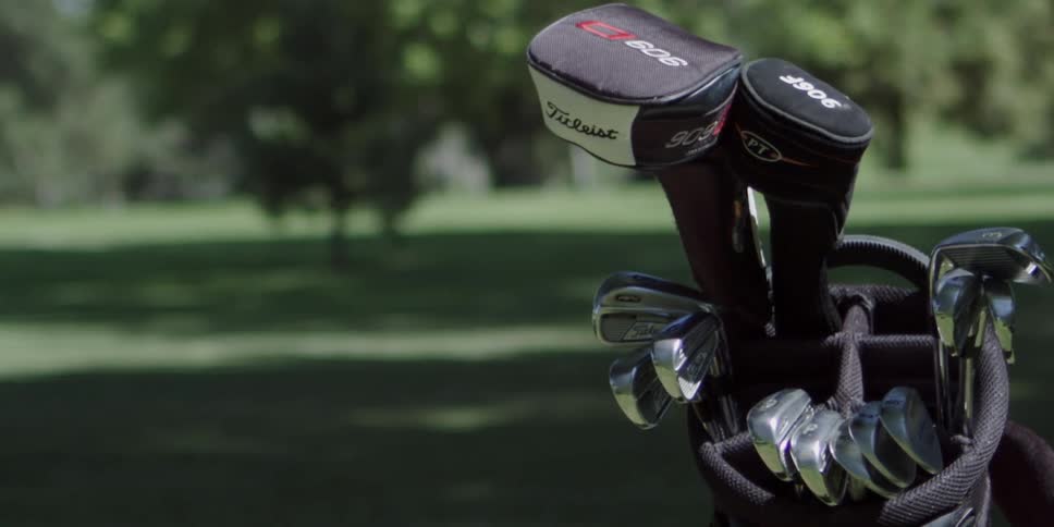 A white man grabs a golf club out of a bag on the course