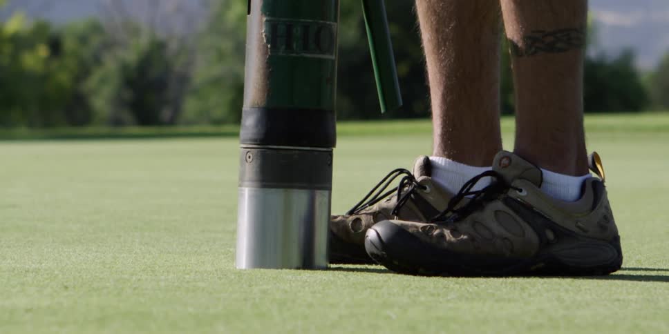 A man stands on a putting green using a machine to dig holes