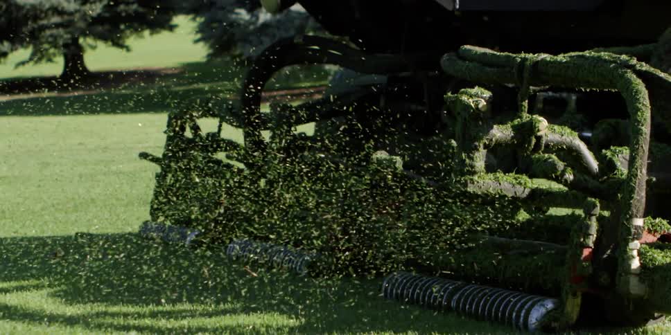 A large riding mower is cutting the grass on the golf course
