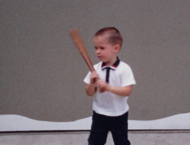 A little boy throws a ball and holds a bat on his driveway