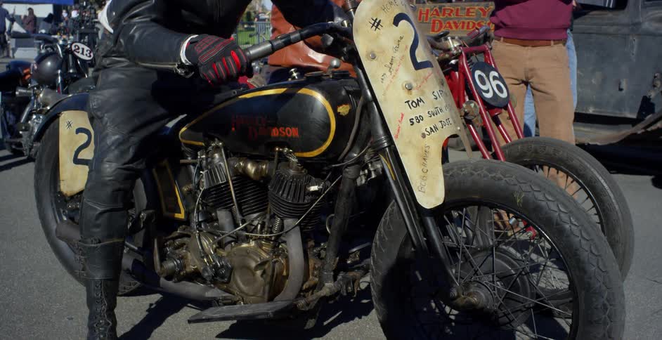 A guy dressed in leather sits on a an old motorcycle at an event