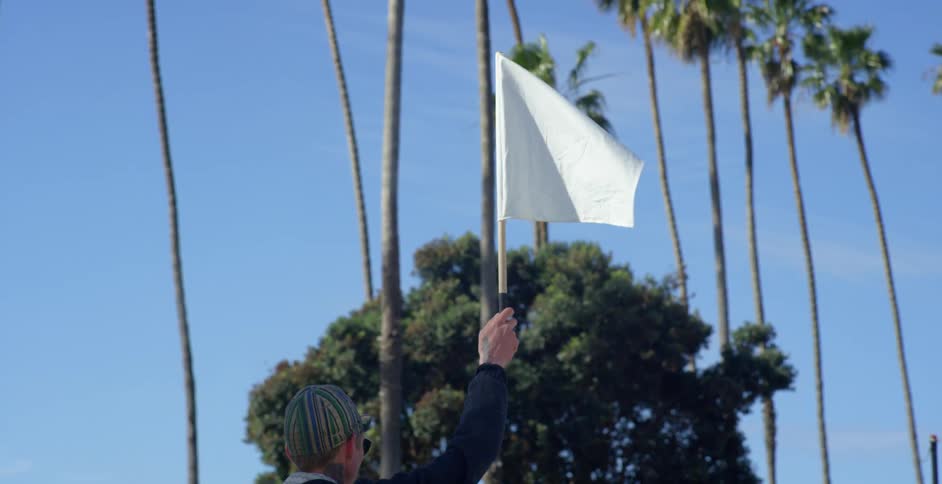 A white man stands outdoors holding up a white flag