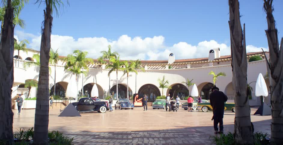 People gather for a small car show in an open air building