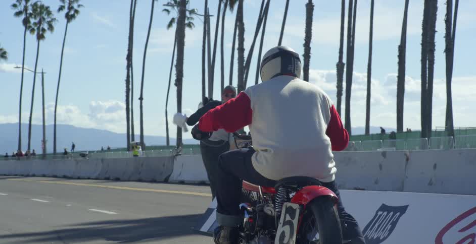 A man on a motorcycle starts to race on a street when a white flag gets thrown