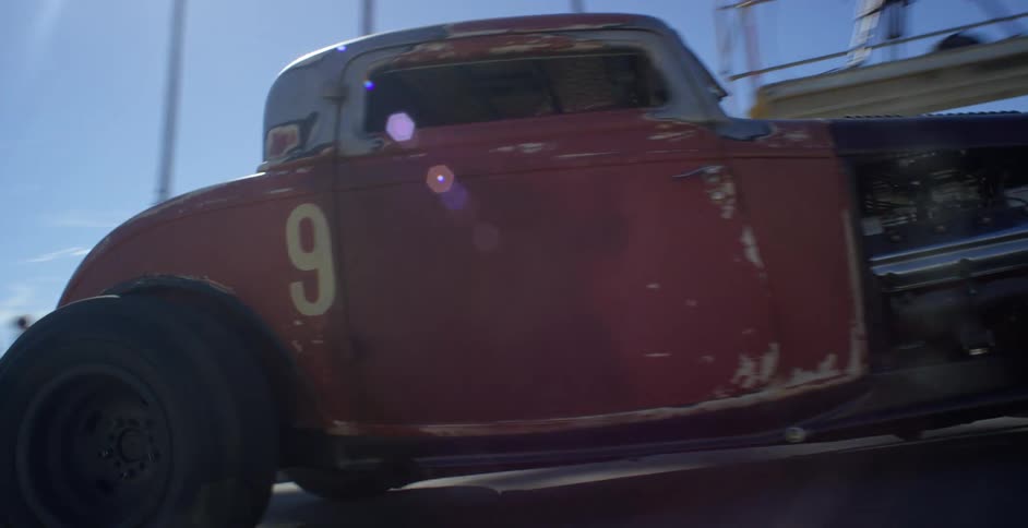 A group of people stand along a track watching a car drive to the start line for a drag race