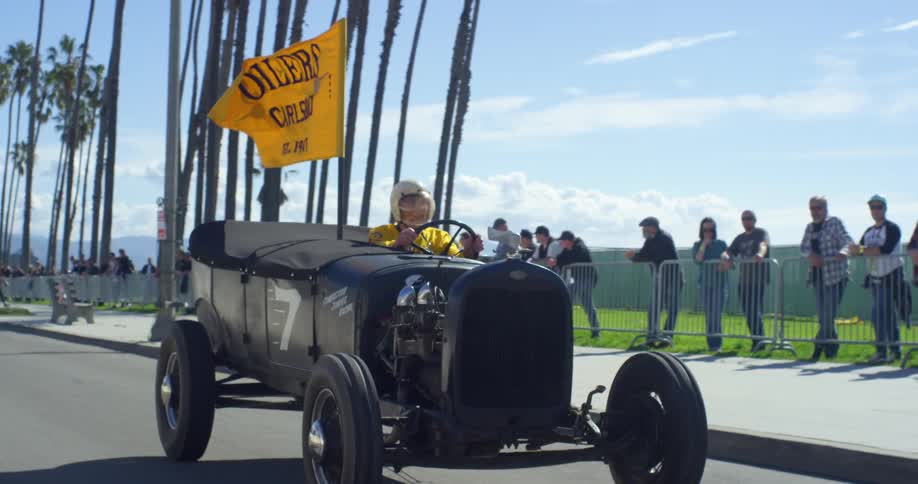 A man drives an old fashioned buggy style go kart equipped with a large flag in a race