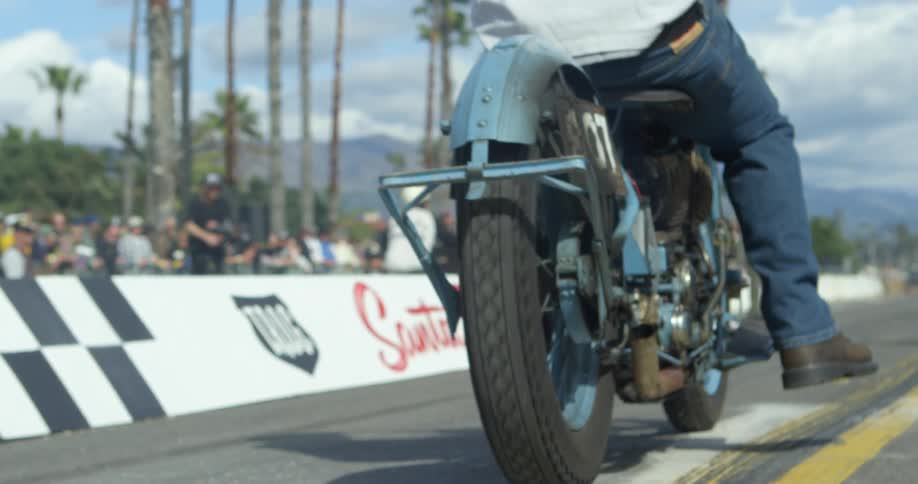 A man on a motorcycle moves forwards as a crowd stands to watch a race