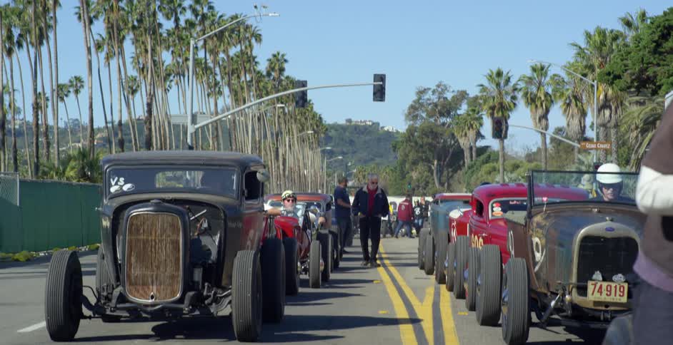 Car enthusiasts check out classic cars lined up and down the road at a car show