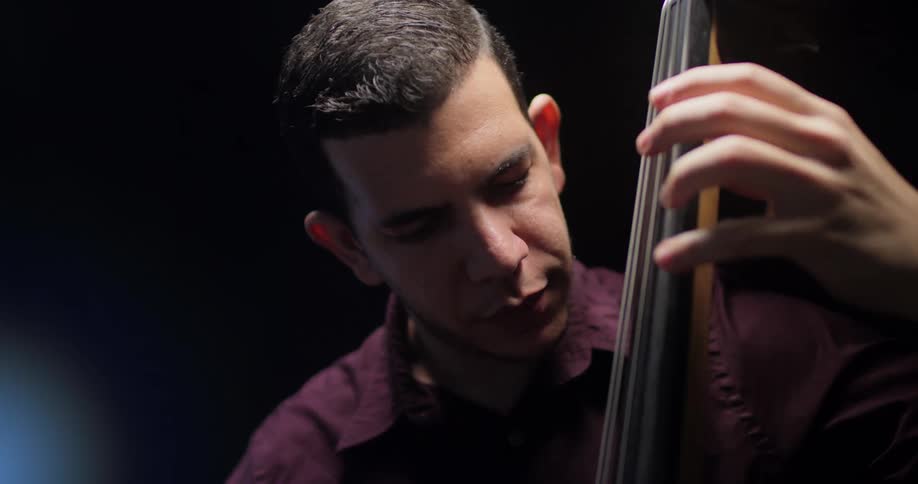 A man is playing an upright bass instrument while standing indoors