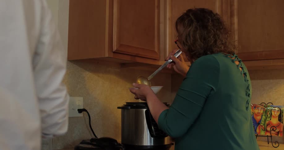 A womans scoops soup from a crock pot into a bowl
