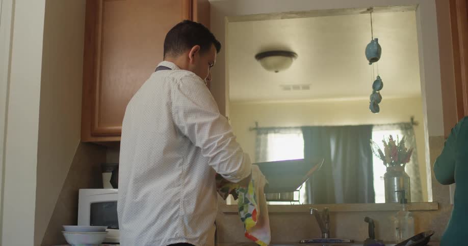 While wife does the dishes husband with a white shirt dries tray in the kitchen
