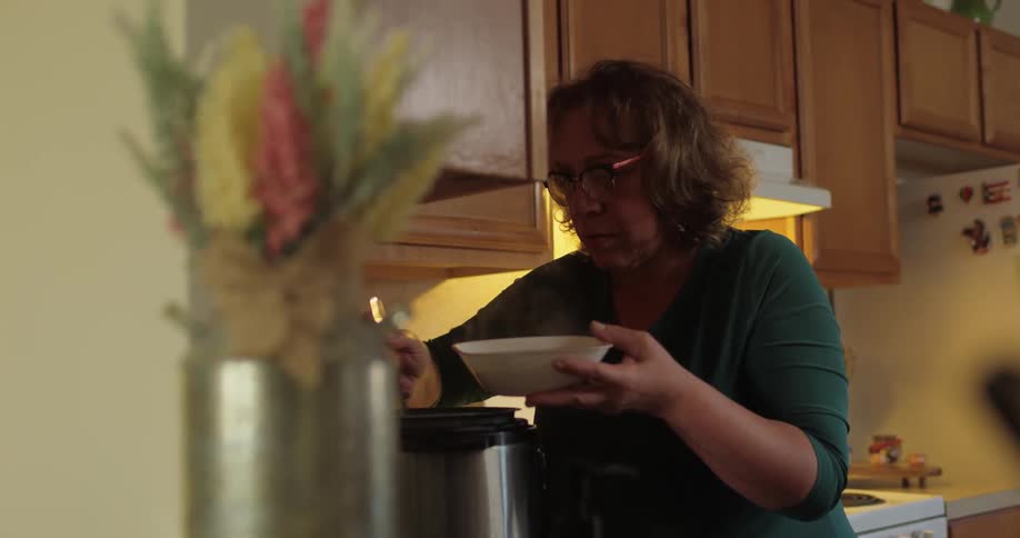 Woman serving a bowl of soup from a pot in the kitchen