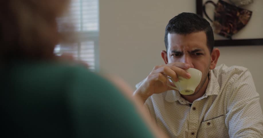 Man drinking tea looking bored while listening to woman talking