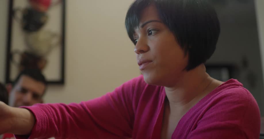 A hispanic woman sits in a house with her family and eats a meal