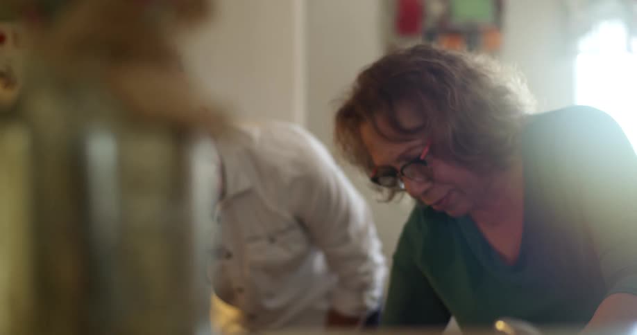 A hispanic women works in a kitchen as a man watches her