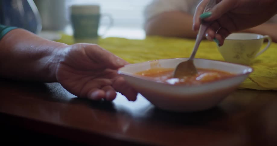 A hispanic family sits at a table while the mother stirs a bowl of food with a spoon