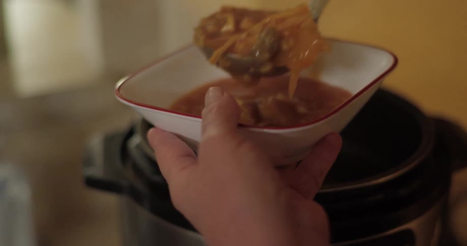 Female holds a bowl next to the crock pot as she uses a ladle to fill the bowl with soup