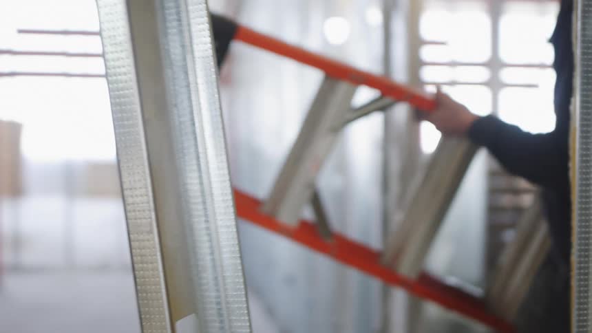 A man carrying a ladder through the steel beams of a construction site