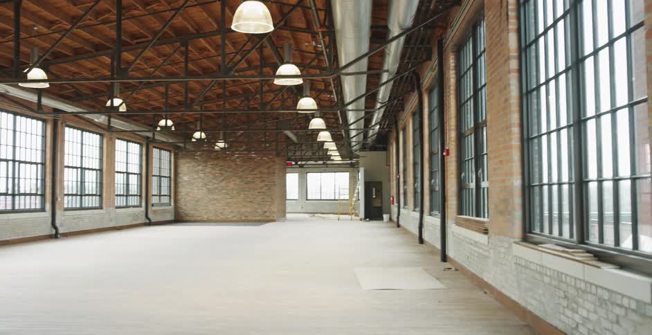 An open loft space with large windows and exposed brick and ceilings in a city