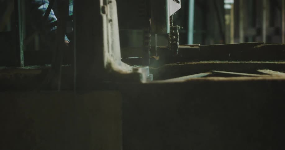 A man works on a beam with large drilling equipment lumber is stacked behind him