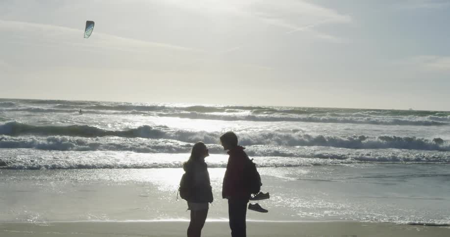 A man and a woman stand on a beach facing each other