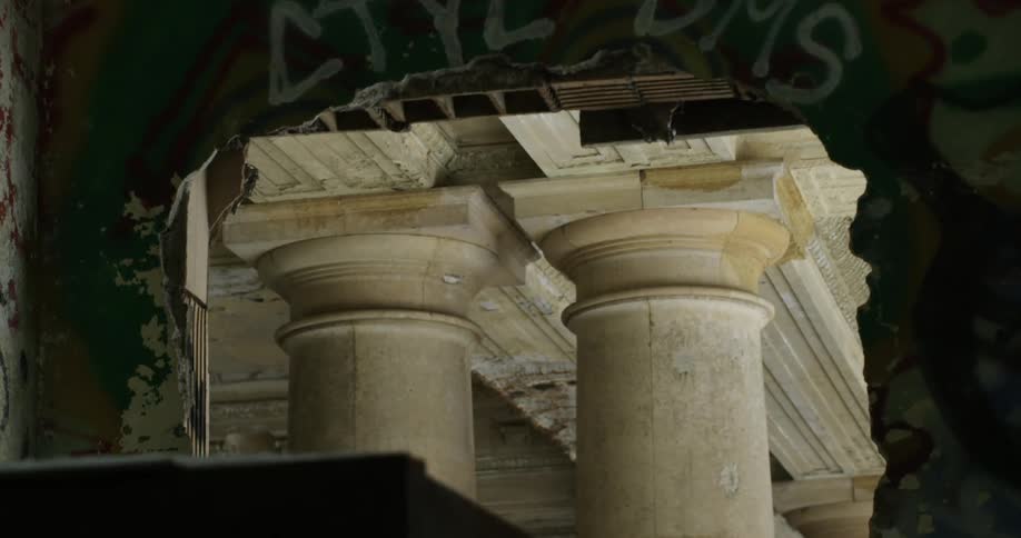 A gaping whole in a building wall reveals giant pillars holding up a ceiling