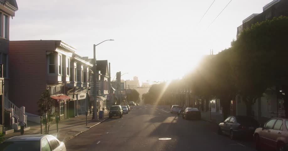 The sun shines down and glares off parked cars on a street running through a small town