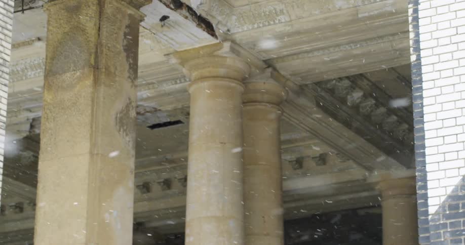 Snowflakes fall outside of an ornate classical style building interior