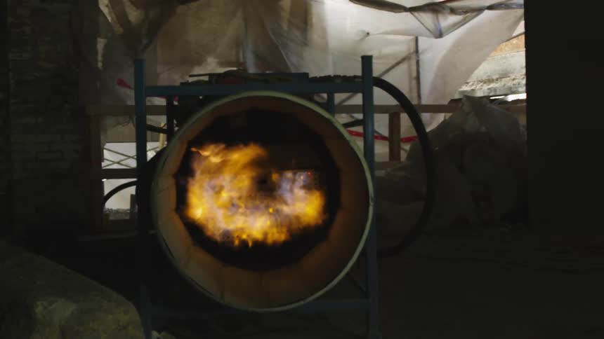 Flames glow bright yellow and orange in a pipe blower equipment in a tarped off construction site