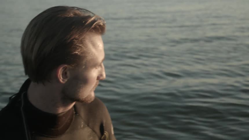 A man sitting on a surfboard runs his hand through his hair