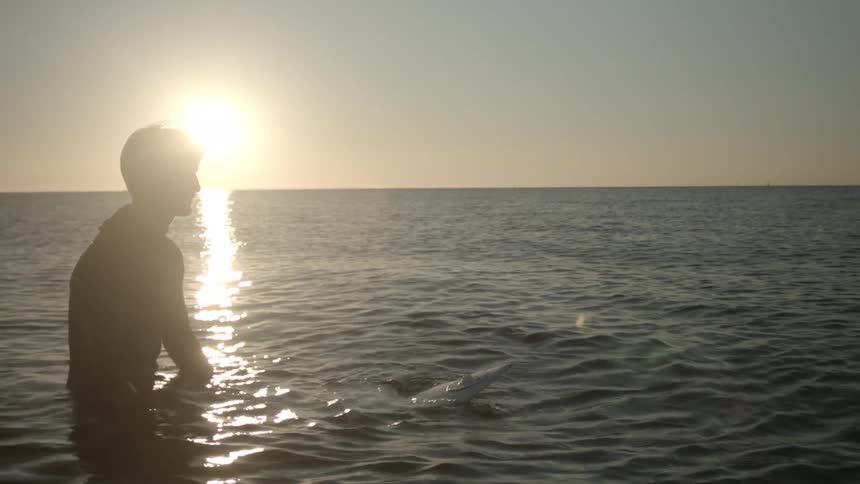 A surfer floats on a surfboard at sunset