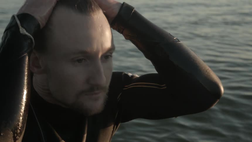 A man in a wet suit smooths back his hair