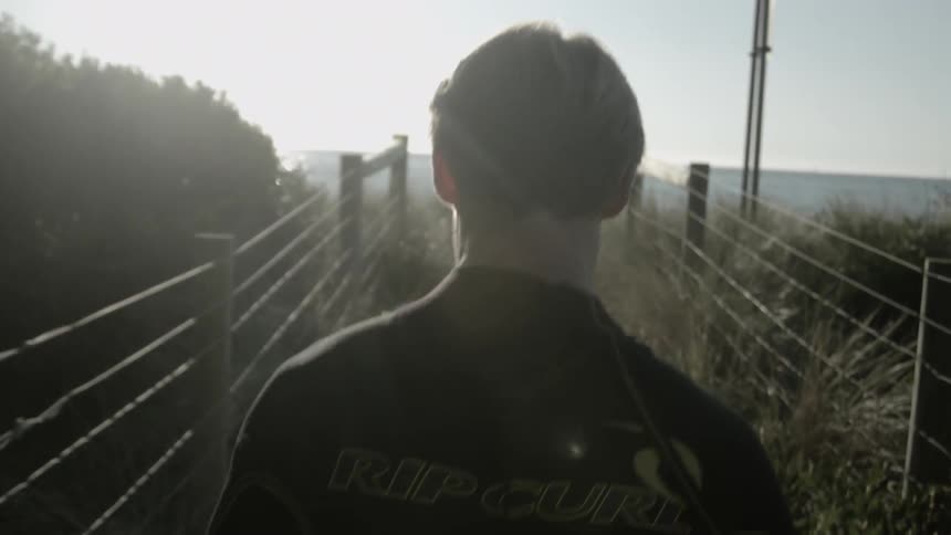 A man is walking down a trail towards the beach