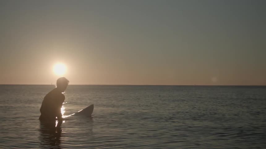 A man is floating on a surfboard watching the sun set