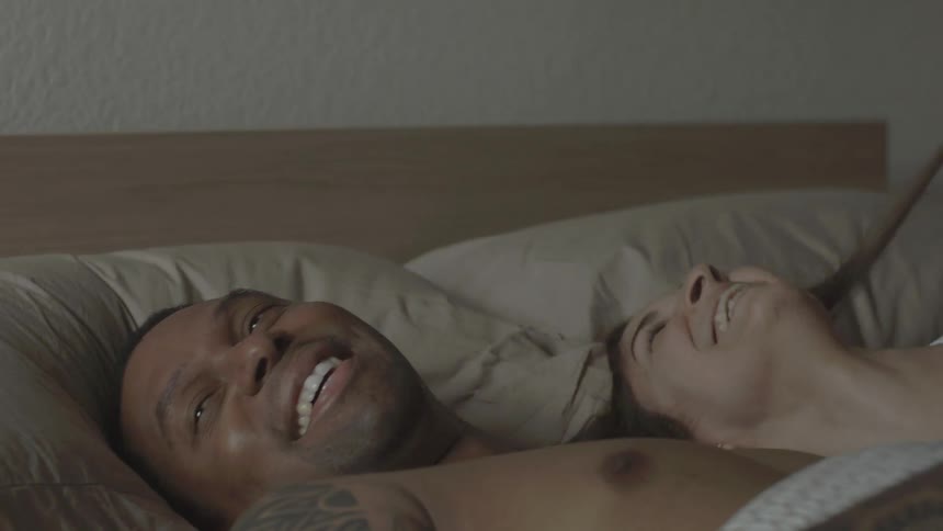 A man and woman are lying in bed laughing and talking