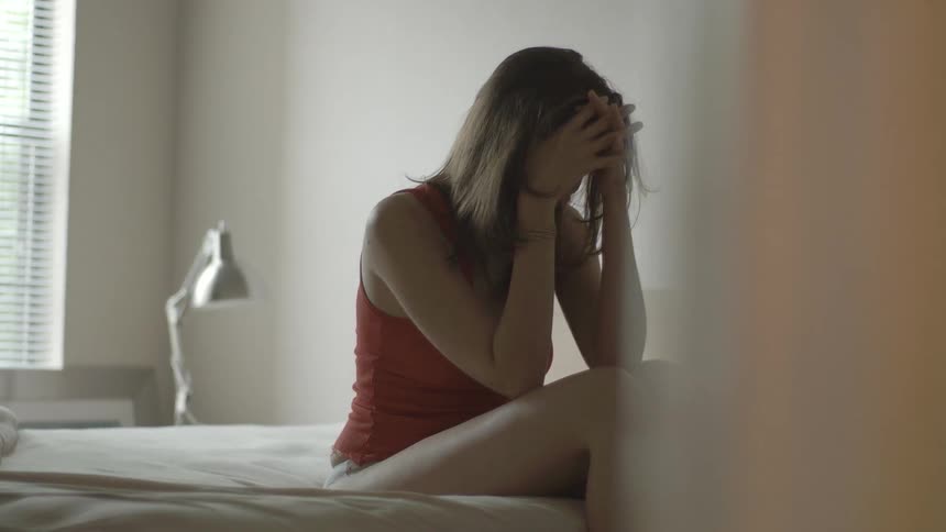 An upset woman sitting on a bed crying