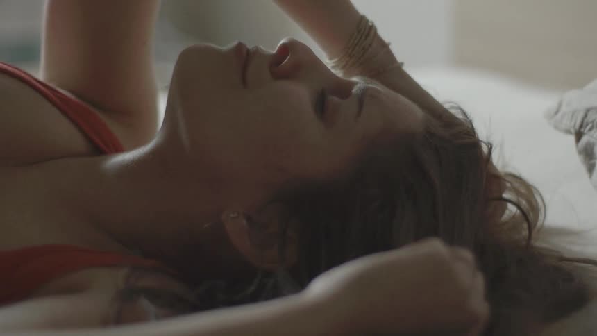 A woman is lying down then slowly puts her hands on her head