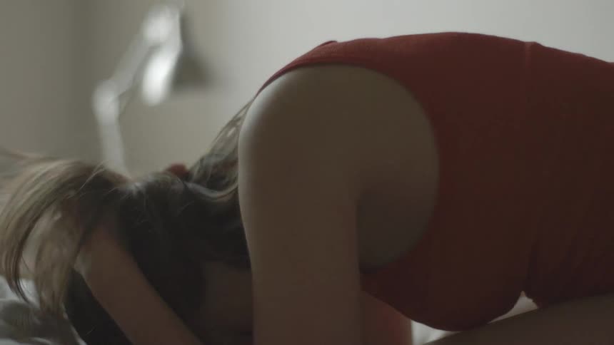 A woman cries into her blankets while on a bed
