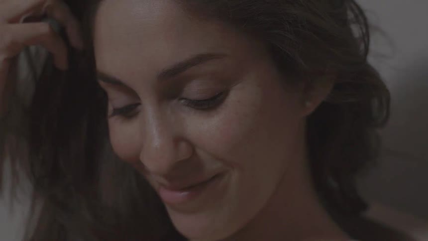 A smiling woman runs her hands playfully through her hair