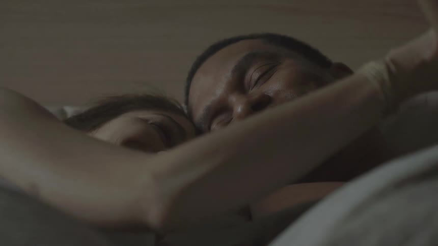 A man and a woman smile in bed and touch each other