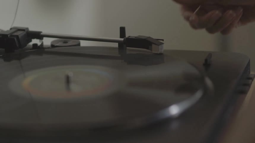 A hand lifts a record player arm and lays it on a spinning record