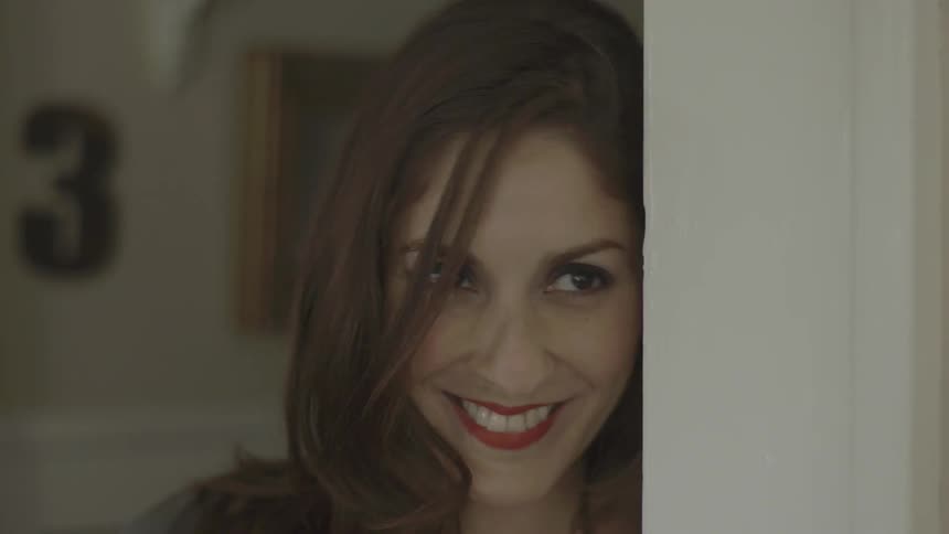 A woman walks around a corner in a home and smiles
