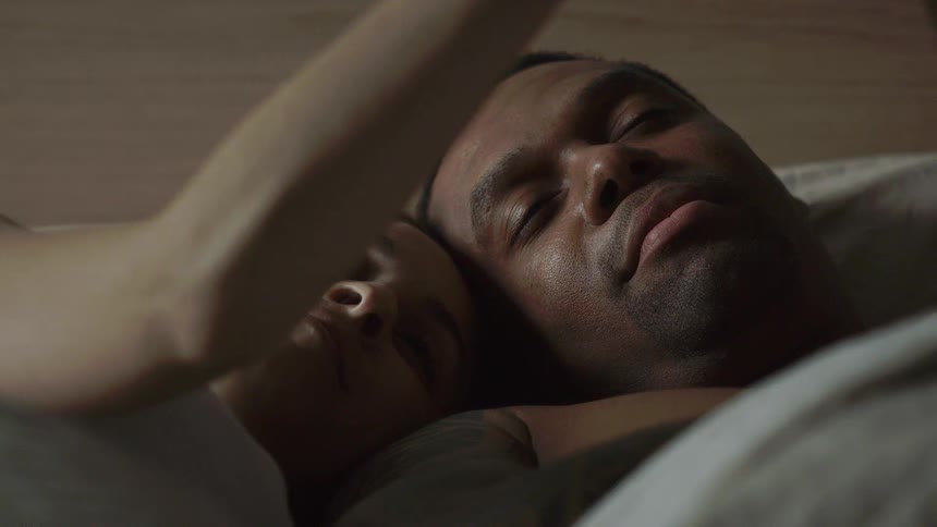 A man and woman lie in bed together talking and laughing