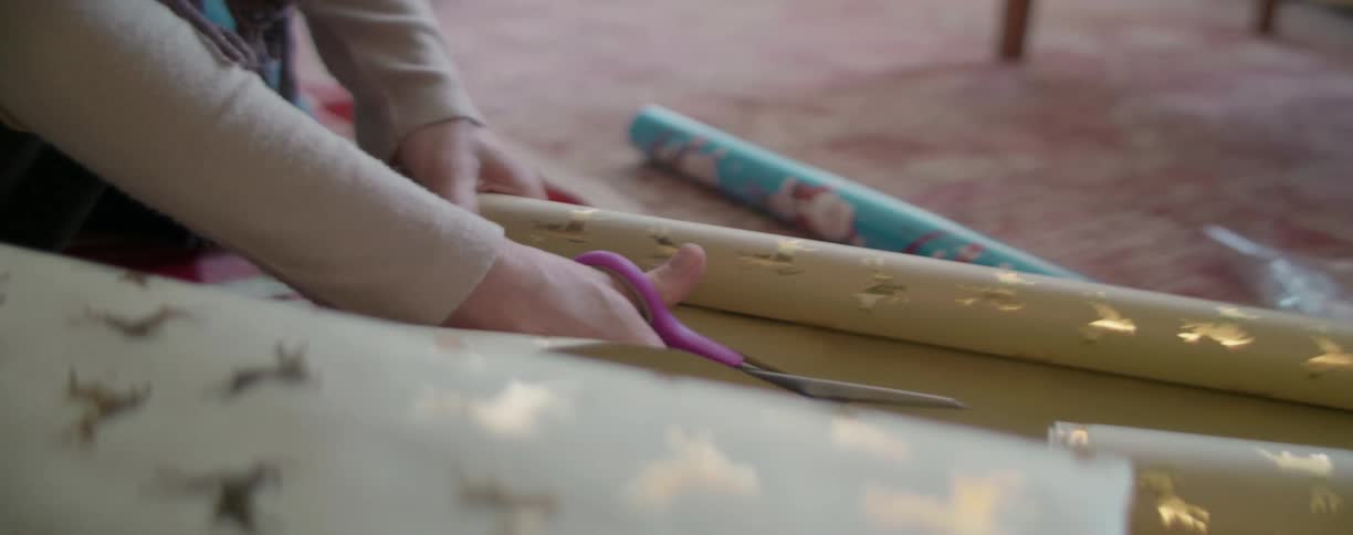 A woman with scissors cutting gift wrapping paper on the floor